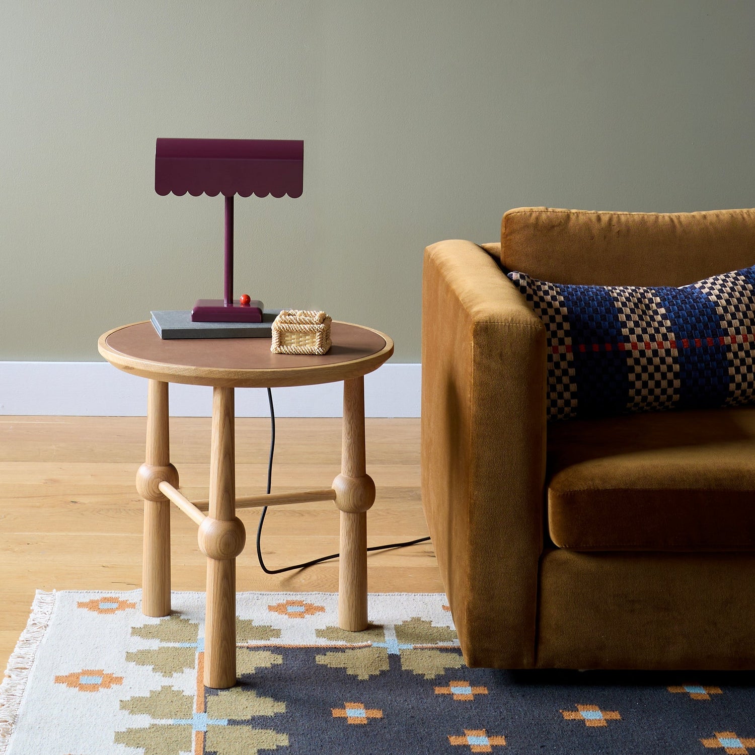 Plaid upholstered armchair beside round wooden side table and oak sideboard in a styled living room with red rug